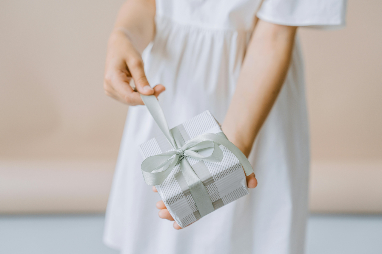 A child in a white dress holds out a small striped gift box tied with a satin ribbon. A child in a white dress holds out a small striped gift box tied with a satin ribbon.