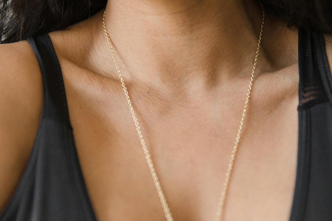 A woman a dainty long yellow gold chain with a pendant out of view.