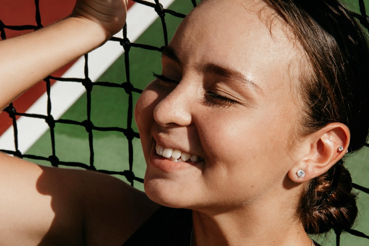 A close-up of a happy young woman wearing stud earrings as she relaxes against a net.