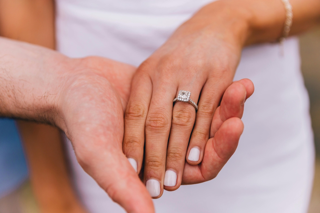 A close-up of a bride-to-be’s hand in her groom’s, with emphasis on her princess-cut engagement ring. A close-up of a bride-to-be’s hand in her groom’s, with emphasis on her princess-cut engagement ring.