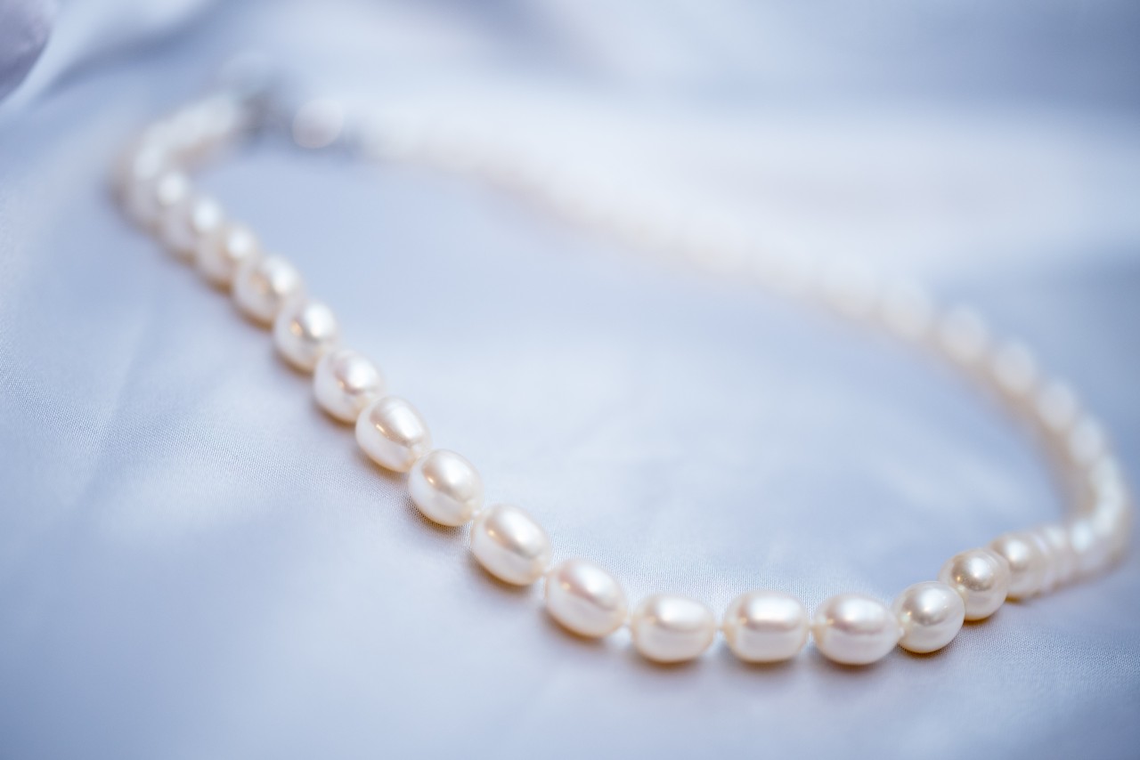 A delicate pearl necklace rests on a smooth, light blue satin fabric. A delicate pearl necklace rests on a smooth, light blue satin fabric.