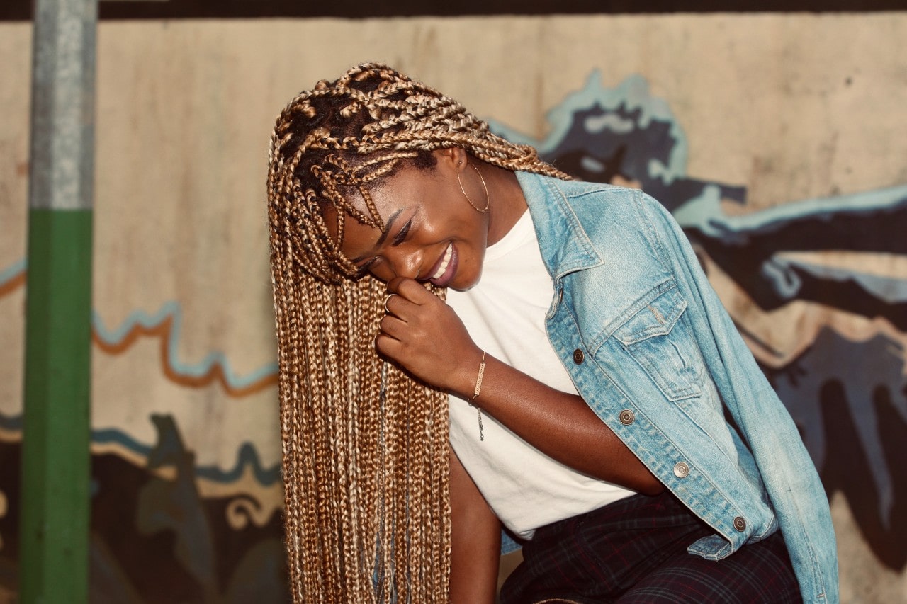 a woman laughing and wearing gold jewelry and a denim jacket