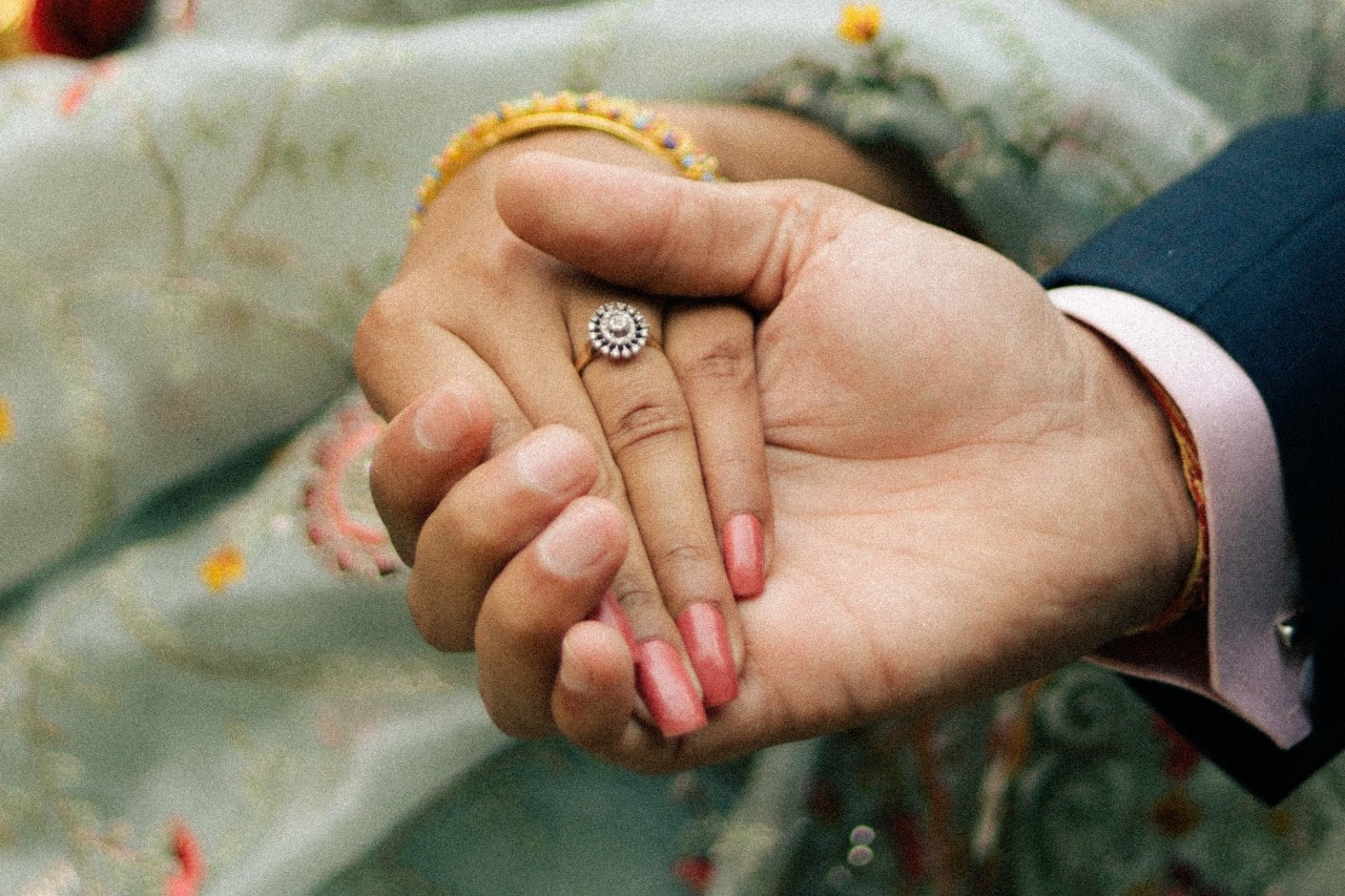 man’s hand holding a lady’s while wearing an engagement ring