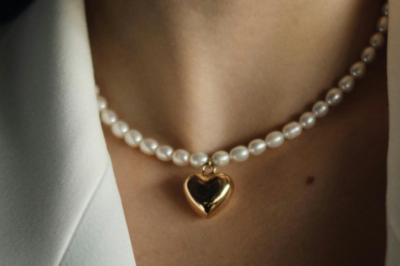 A close up of a pear necklace with a gold heart pendant on a woman’s neck