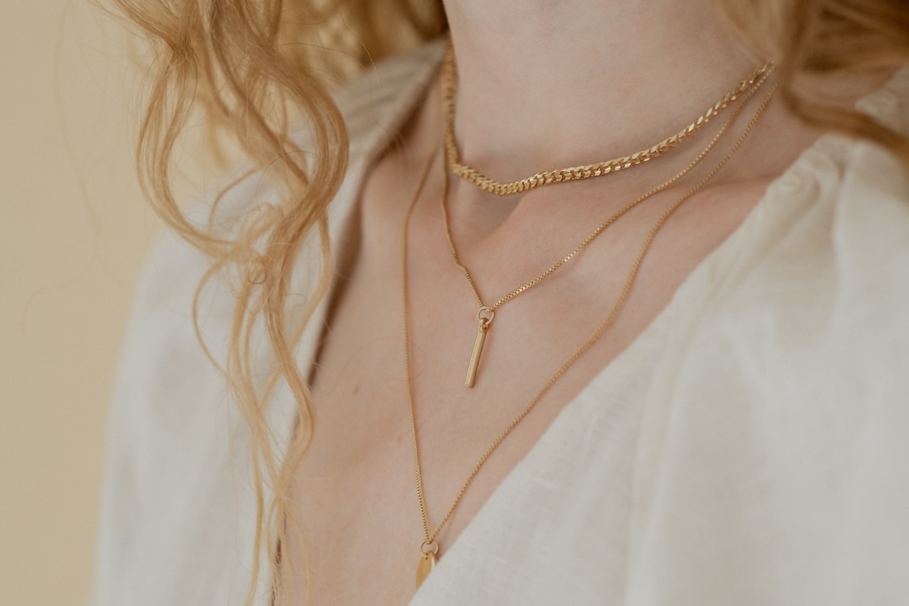 close up image of a woman’s neck, adorned with three gold necklaces of varying lengths close up image of a woman’s neck, adorned with three gold necklaces of varying lengths
