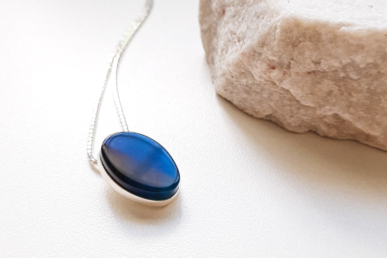 a white gold pendant necklace with a deep blue gemstone on a white surface