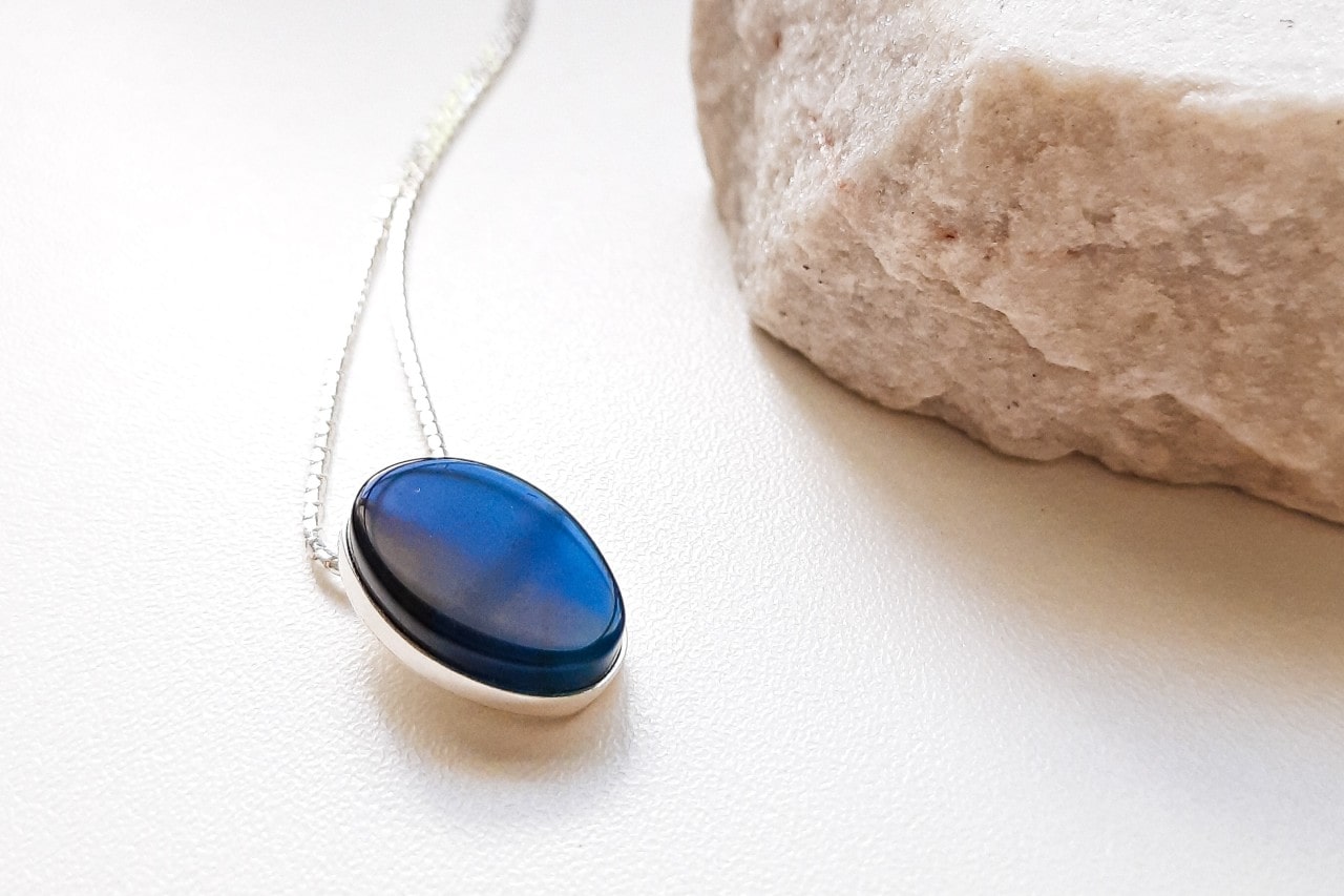 a white gold pendant necklace with a deep blue gemstone on a white surface a white gold pendant necklace with a deep blue gemstone on a white surface