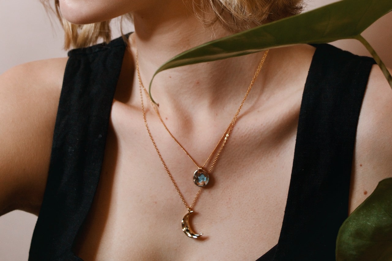 close up image of a woman’s chest, adorned with two yellow gold pendant necklaces close up image of a woman’s chest, adorned with two yellow gold pendant necklaces