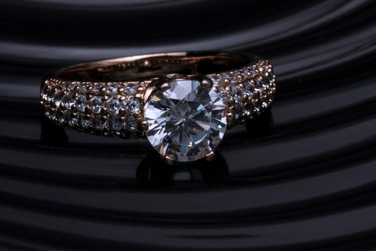 A luxurious diamond engagement ring set in rose gold, featuring a large round-cut diamond surrounded by smaller diamonds on the band A luxurious diamond engagement ring set in rose gold, featuring a large round-cut diamond surrounded by smaller diamonds on the band