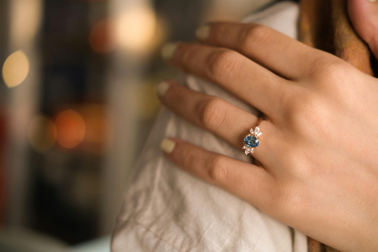 A close-up of a woman's hand wearing an elegant engagement ring with a blue sapphire center stone, surrounded by small diamonds A close-up of a woman's hand wearing an elegant engagement ring with a blue sapphire center stone, surrounded by small diamonds