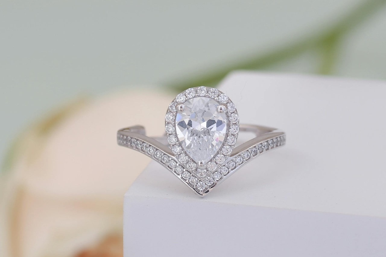 A modern halo pear-cut diamond engagement ring sits at the edge of a table.